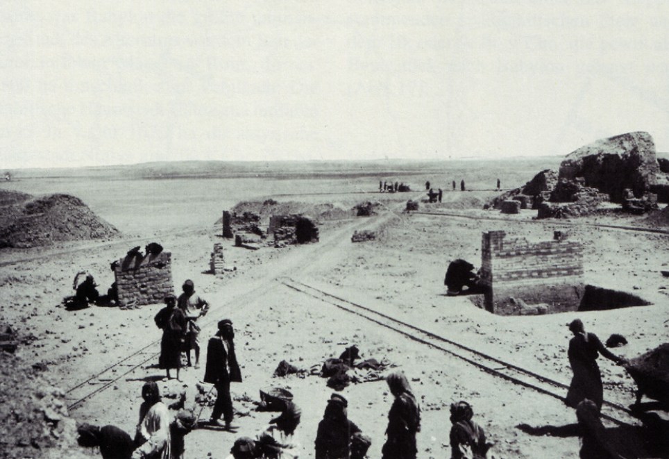 Menschen, die 1902 an den Ausgrabungen arbeiten, sich bücken, mit einer Feldbahn Ausgrabungsstücke transportieren (Schwarz-Weiß-Aufnahme)